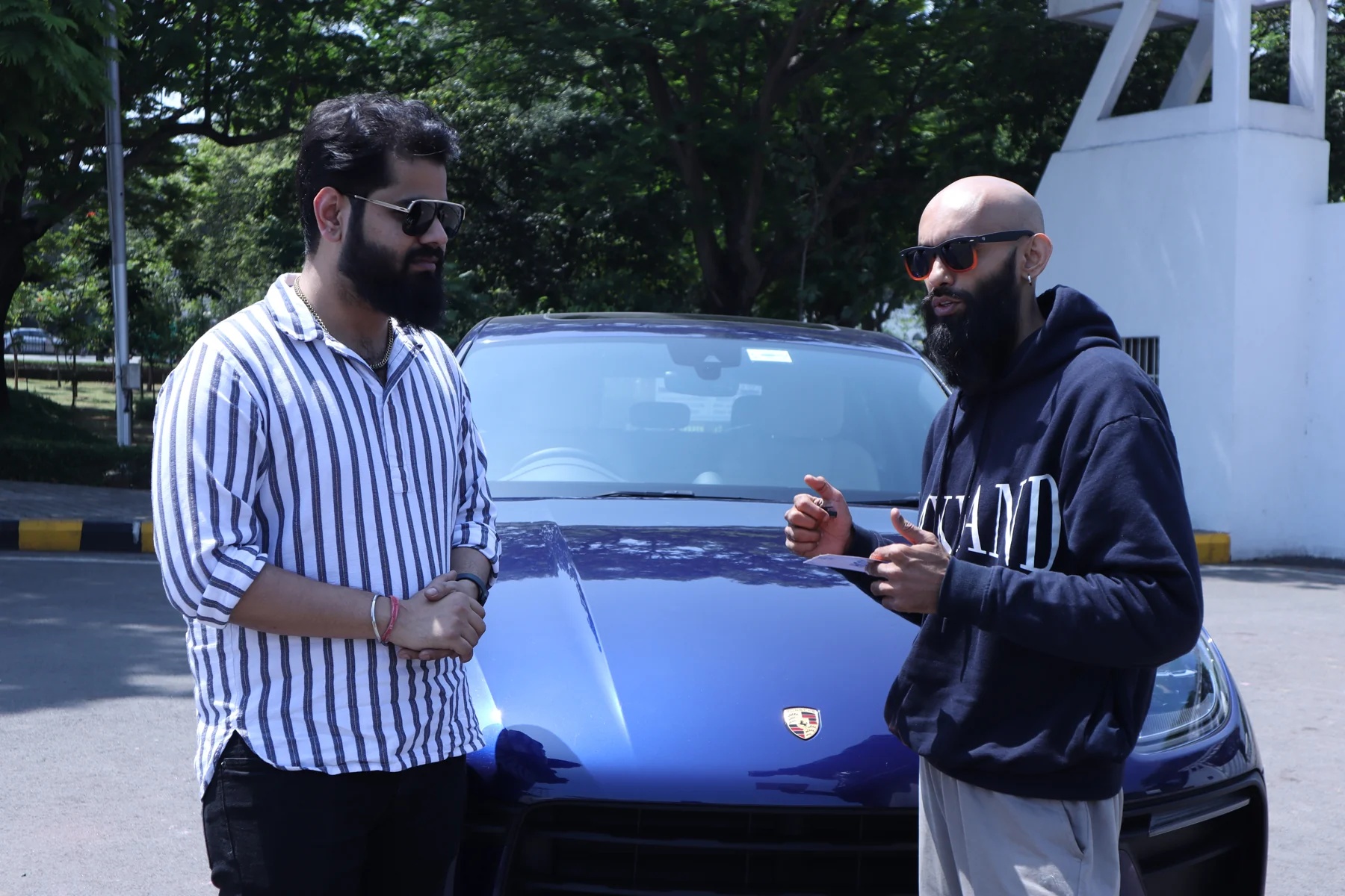 Two men talking beside the bonnet of the blue Porsche during the film shoot