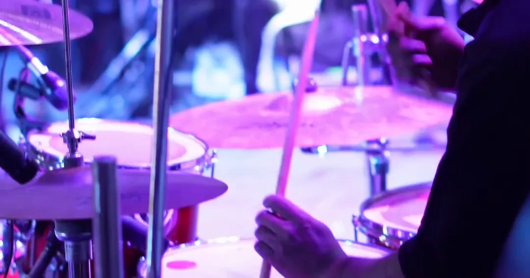 The drummer playing under purple stage lighting