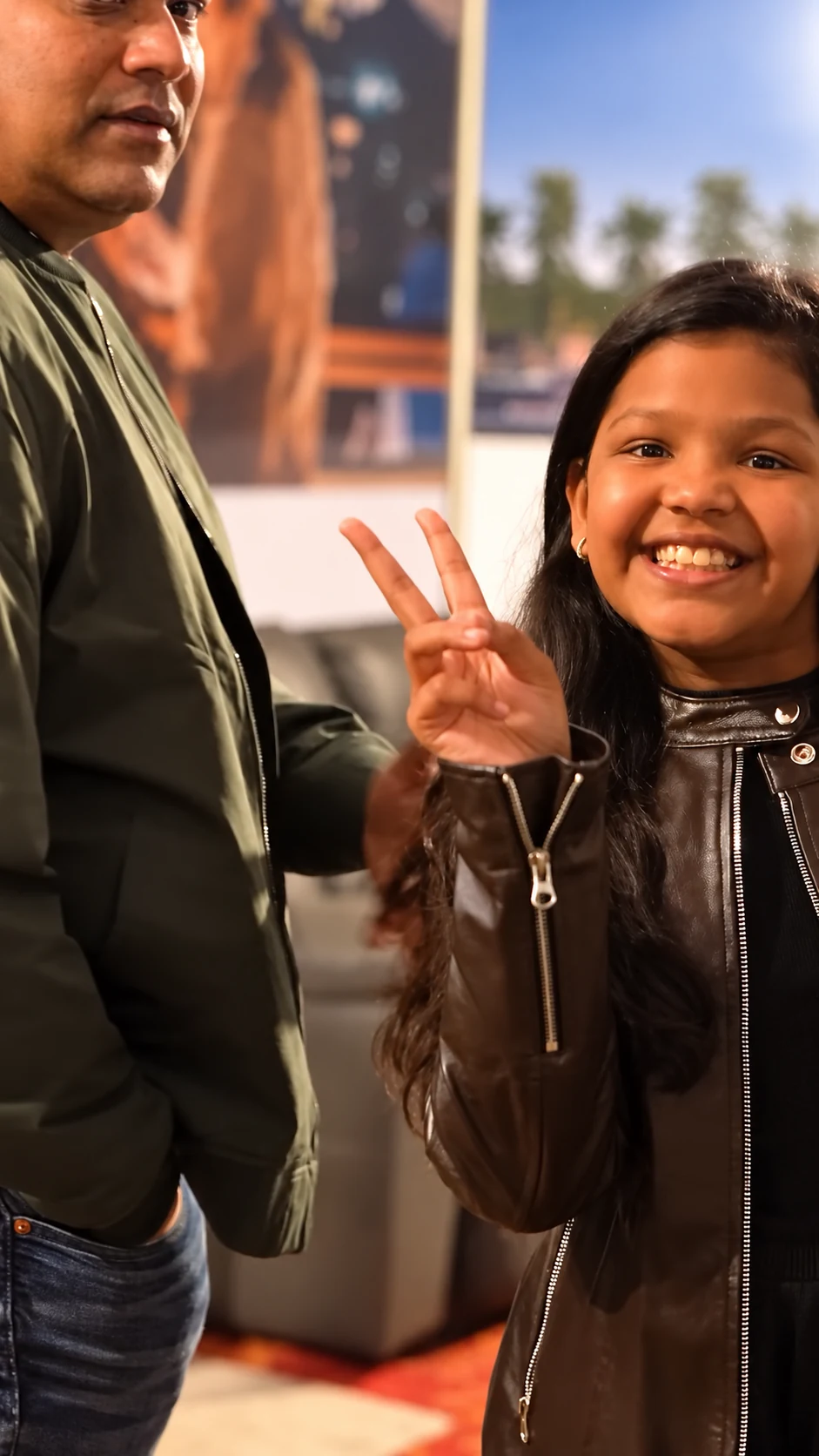 A smiling girl making a peace gesture beside an adult at Hakuna Matata