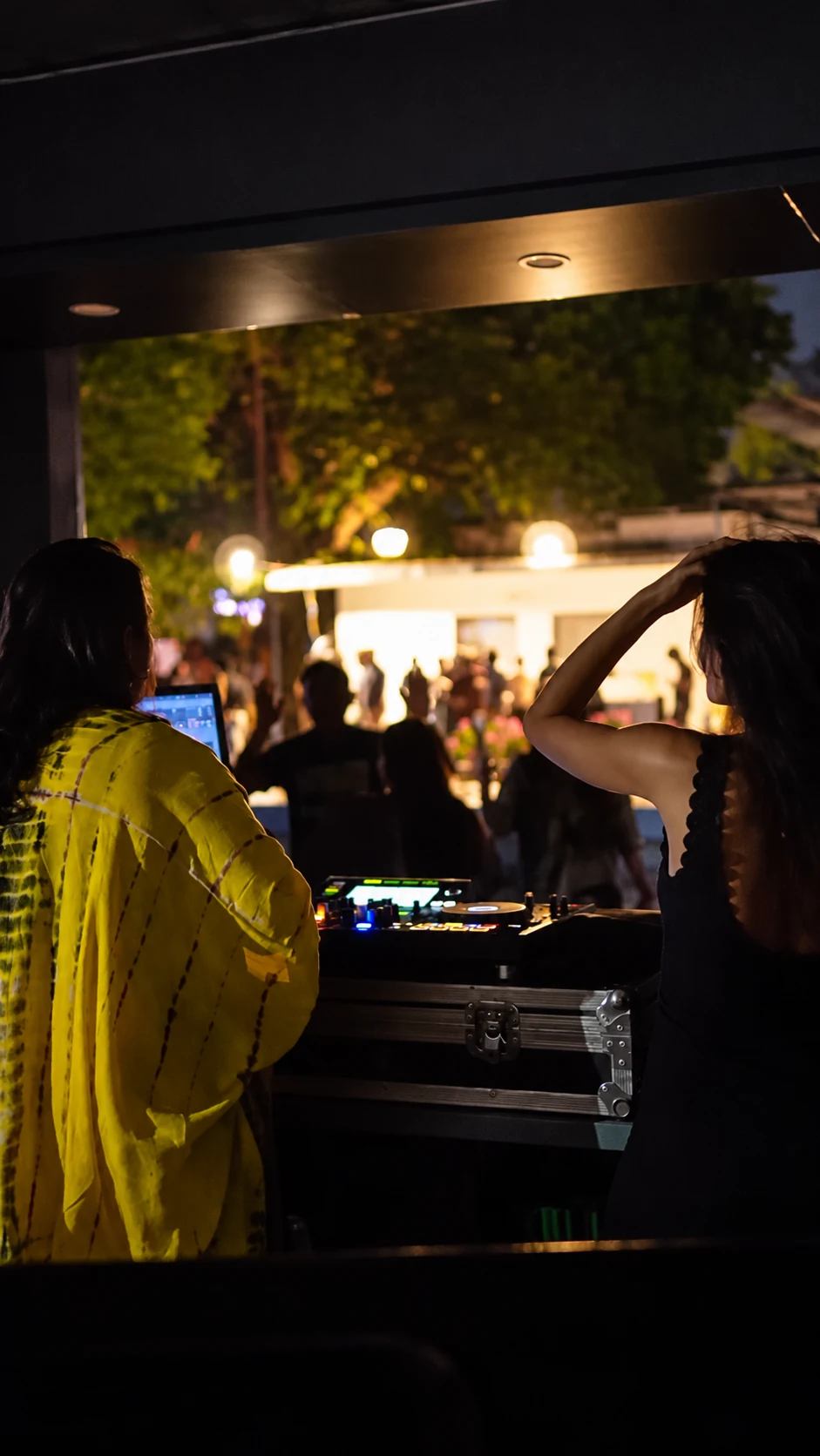 Two people beside the DJ equipment with the party beyond them