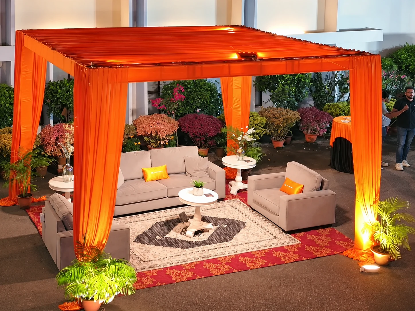 Sofas and armchairs arranged under an orange canopy, with orange cushions and tables