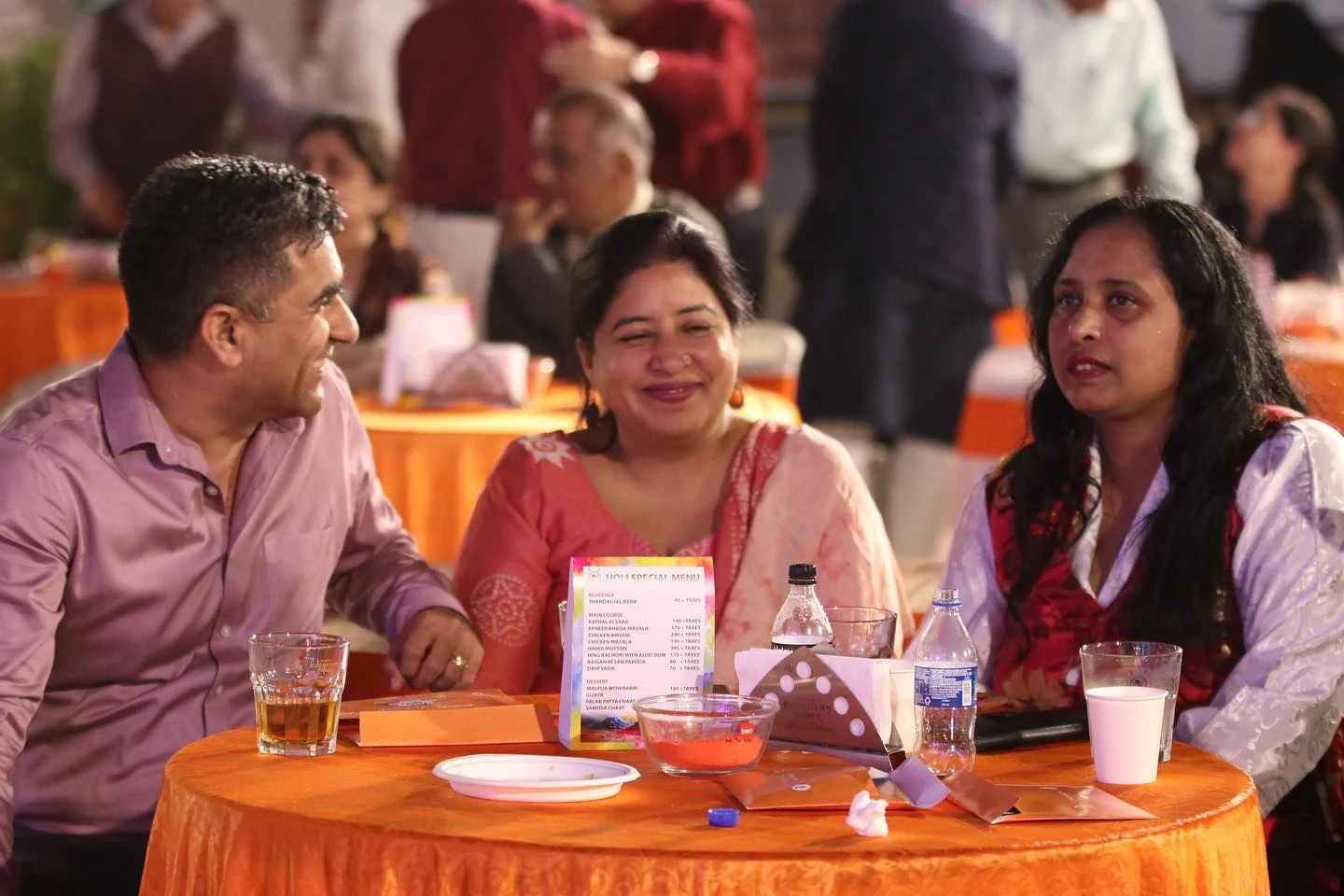 A man and two women seated in conversation around an orange-covered table at the event