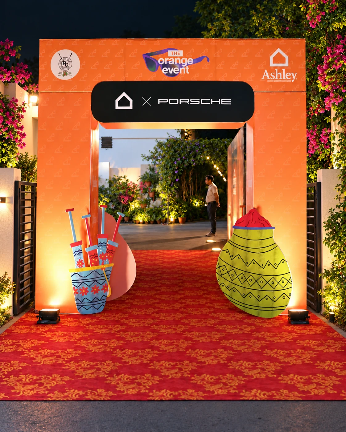 The orange event entrance with Ashley and Porsche branding, framed by flowers and a red carpet