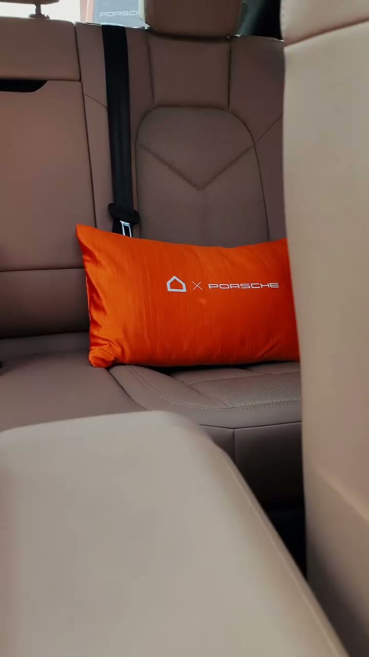 An orange cushion bearing the Ashley house mark and Porsche name on the beige rear seat of a car