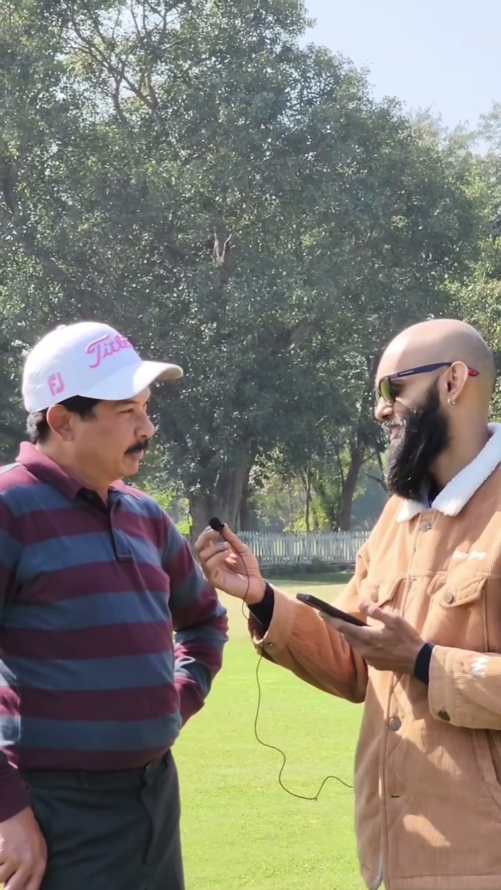 The bearded creator holding a microphone while interviewing a golfer on the course