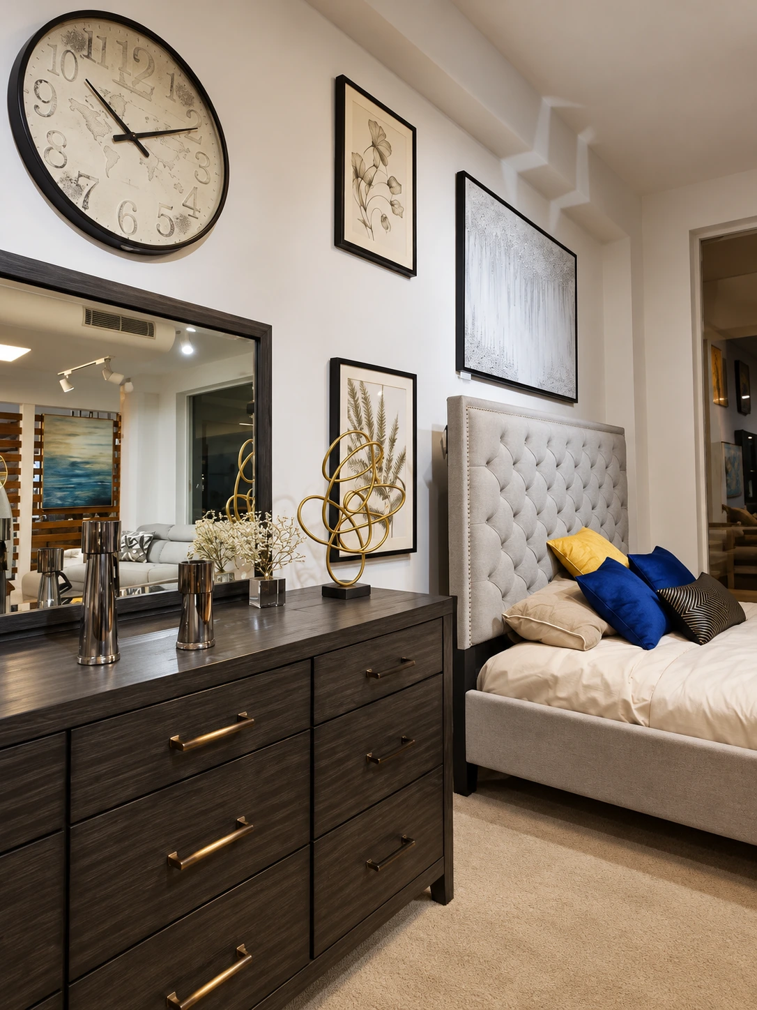 An upholstered bed with blue and yellow cushions beside a dark wooden dresser and mirror