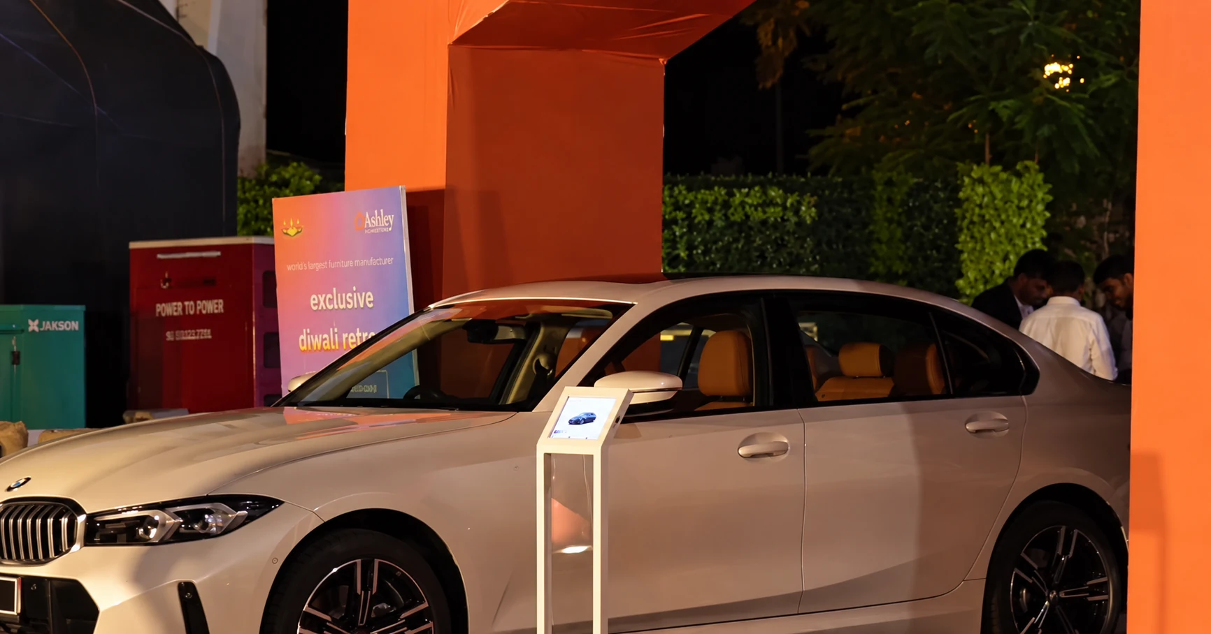 A white BMW beneath the orange event structure beside the physical Ashley event standee