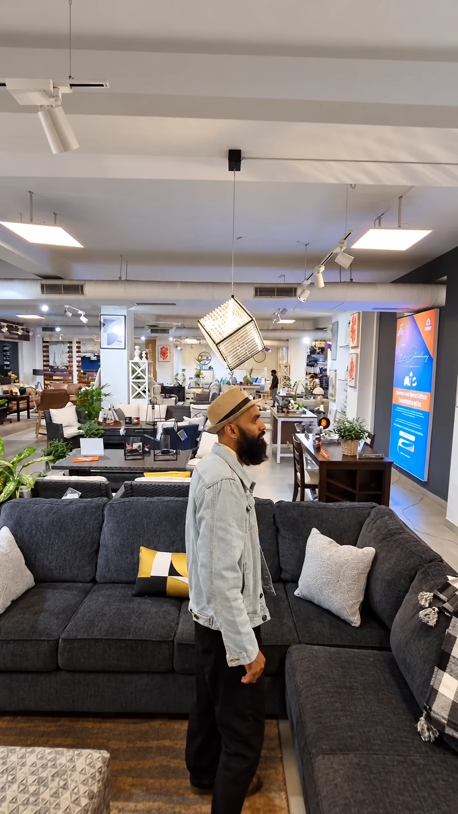 The creator walking beside a dark sofa and looking across the showroom’s furniture settings
